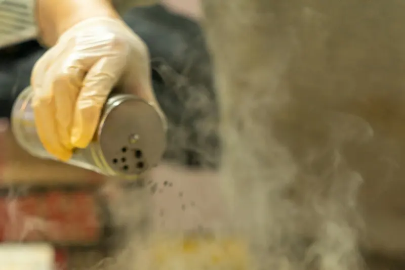 Une main assaisonne une crêpe sur la crêpière, dans la vapeur