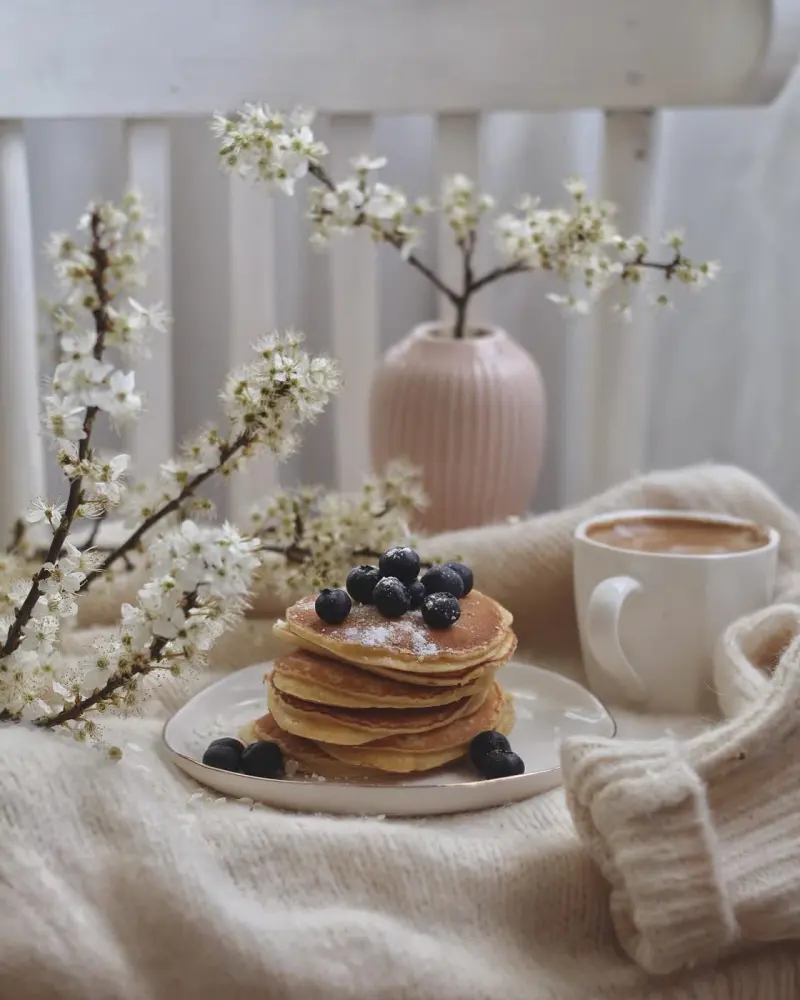 Pile de crêpes, tasse de café et branches fleuries